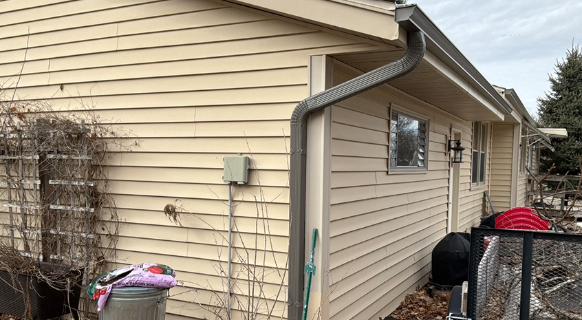 Installer fastening new seamless gutters along a light-colored residential roofline