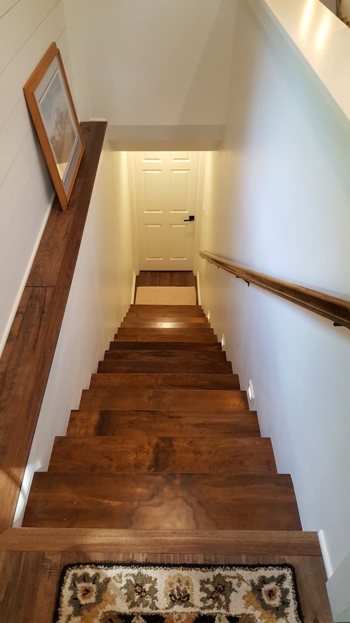 Remodeled wooden staircase with white risers and stained handrail in hallway