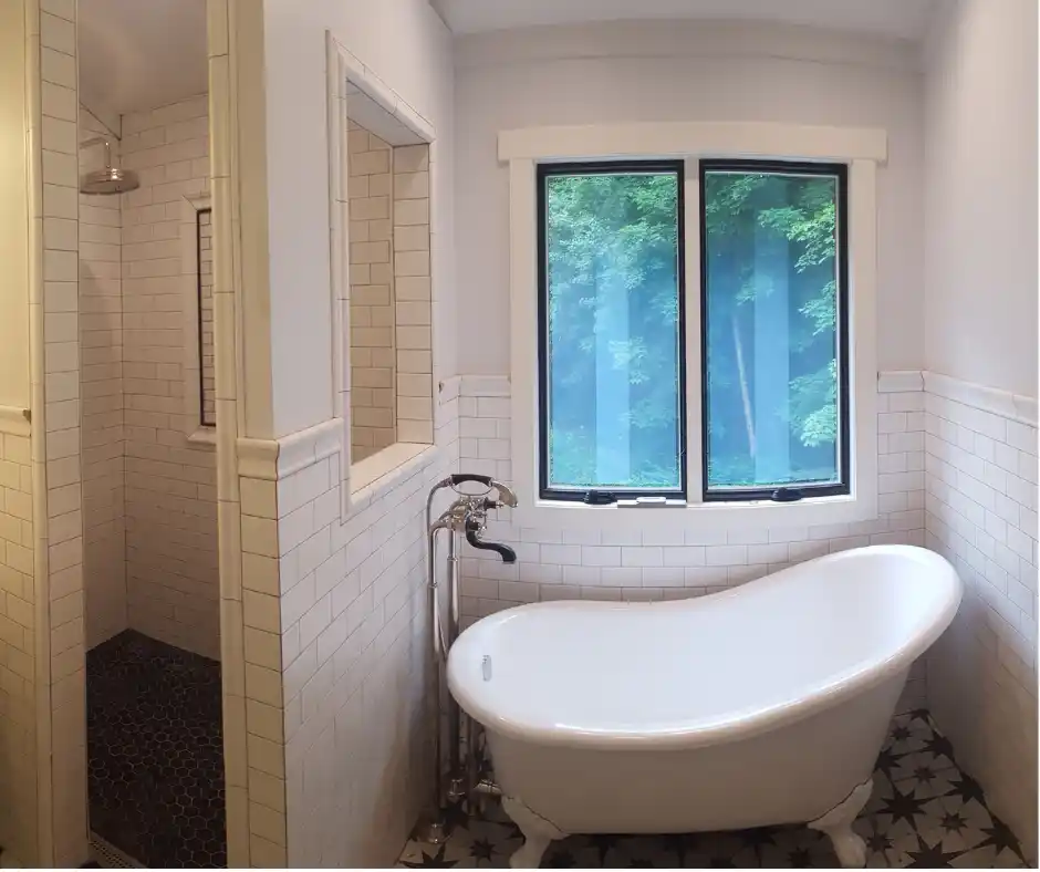 White freestanding bathtub positioned beneath a large window with natural light